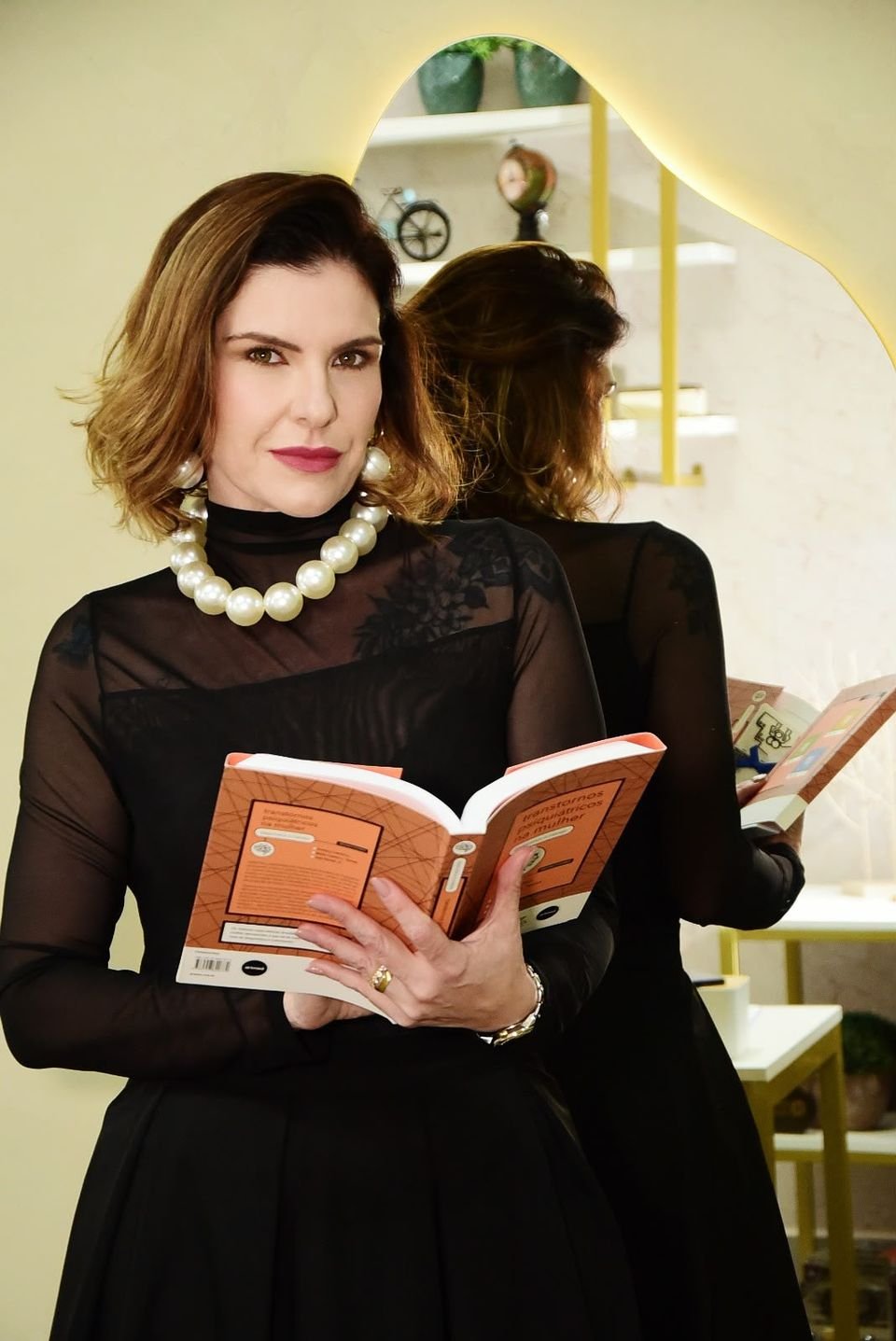 Dra. Ana Carla Prado lendo um livro, sentada no consultório