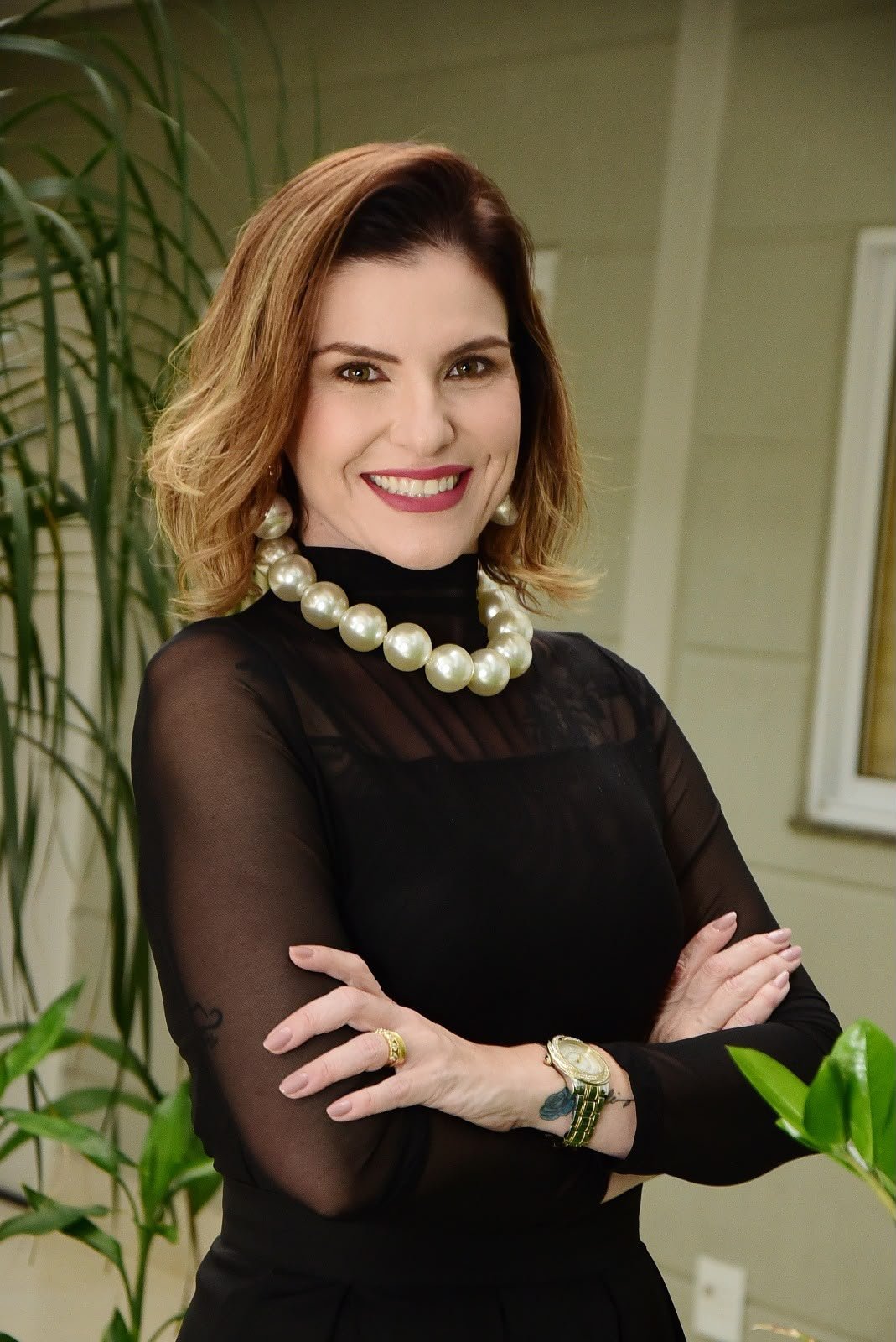 Dra. Ana Carla Prado sorrindo, de braços cruzados, próxima às plantas